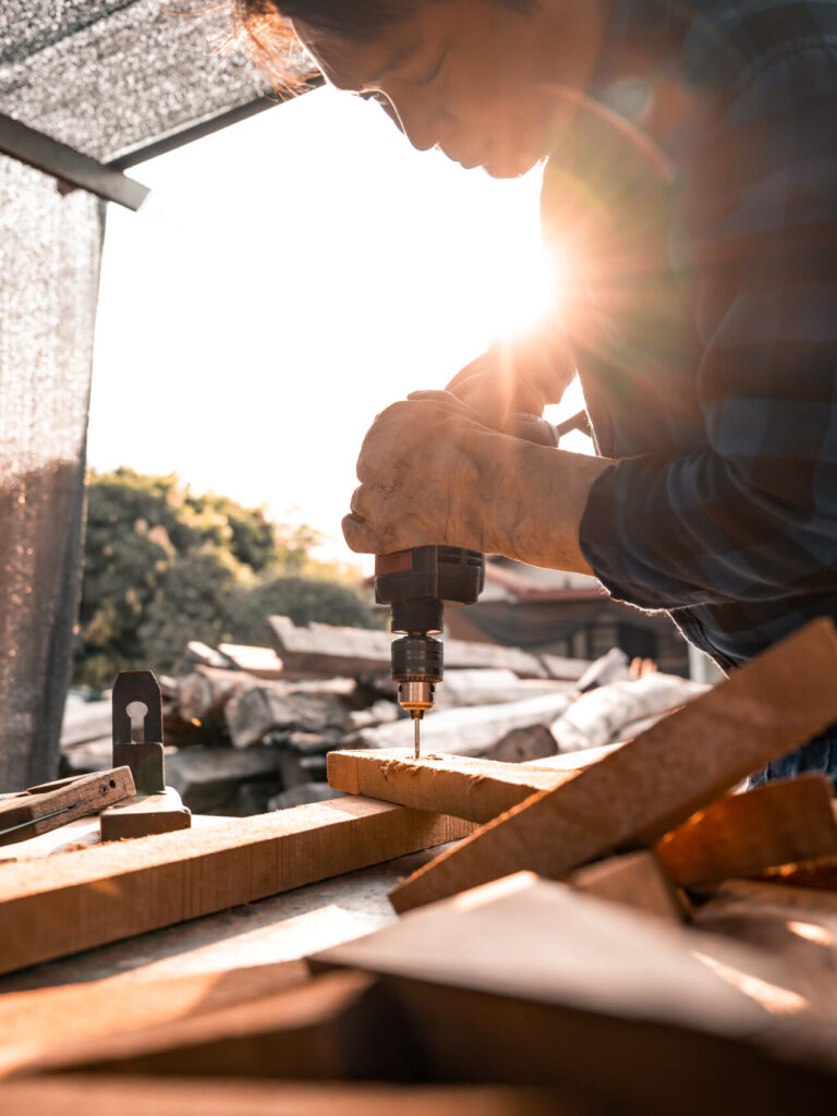Close-up view A carpenter using a drilling tool or an electric screwdriver is working at home on the wooden floor. Ideas for home improvement and extension.